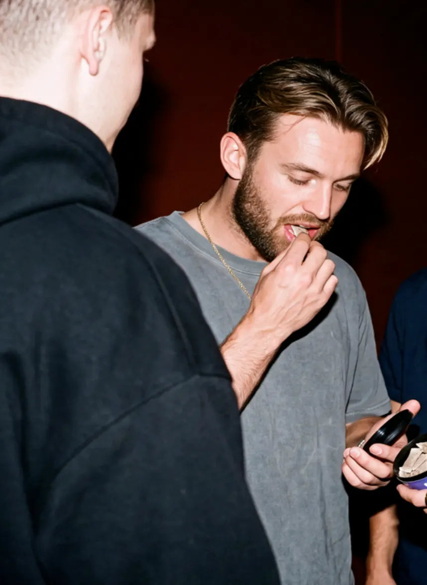 Jonge man die op een feestje een WAVE-pouch onder zijn lip doet