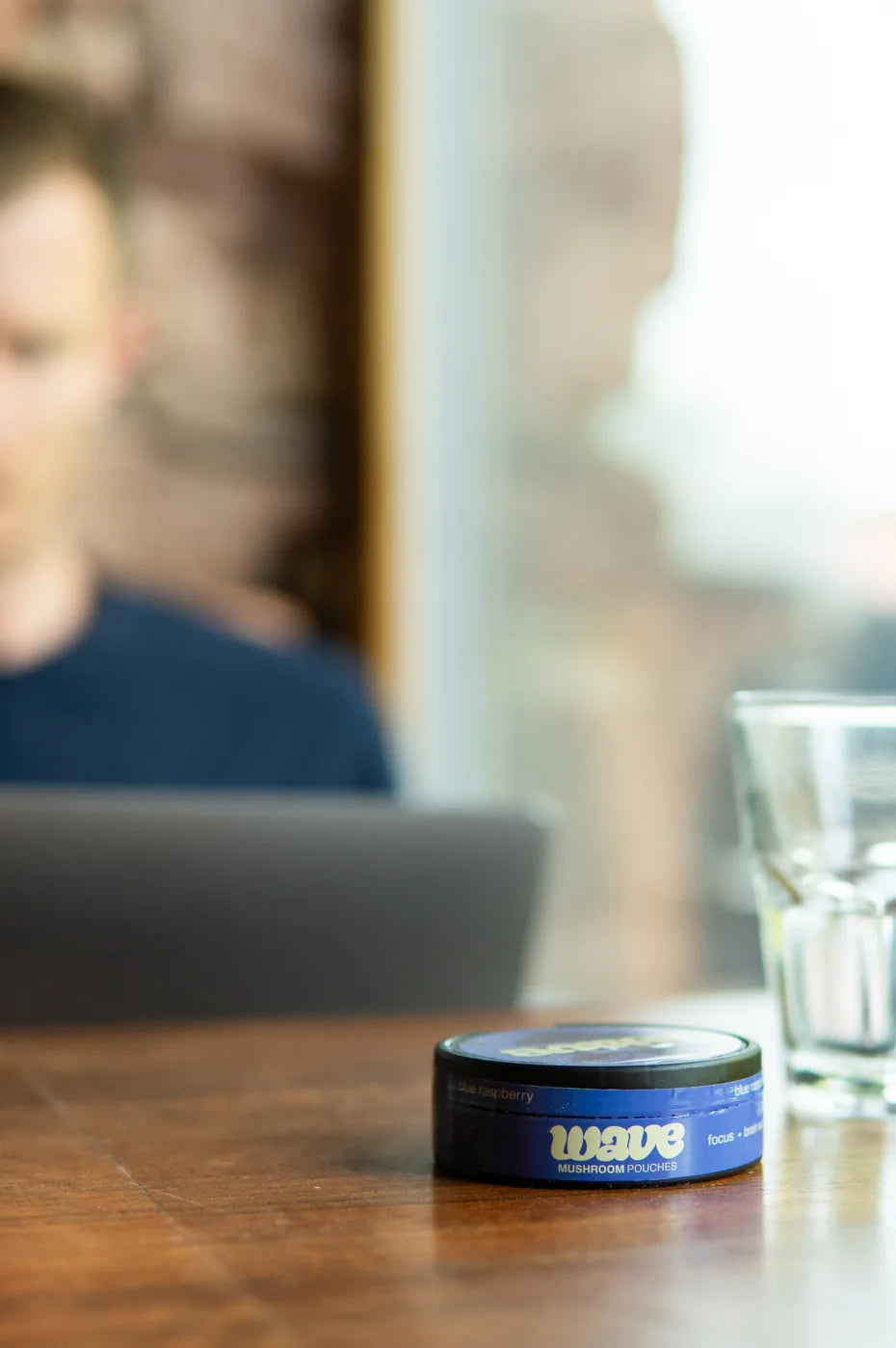 Blikje WAVE op een houten cafétafel, op de achtergrond een man met een laptop