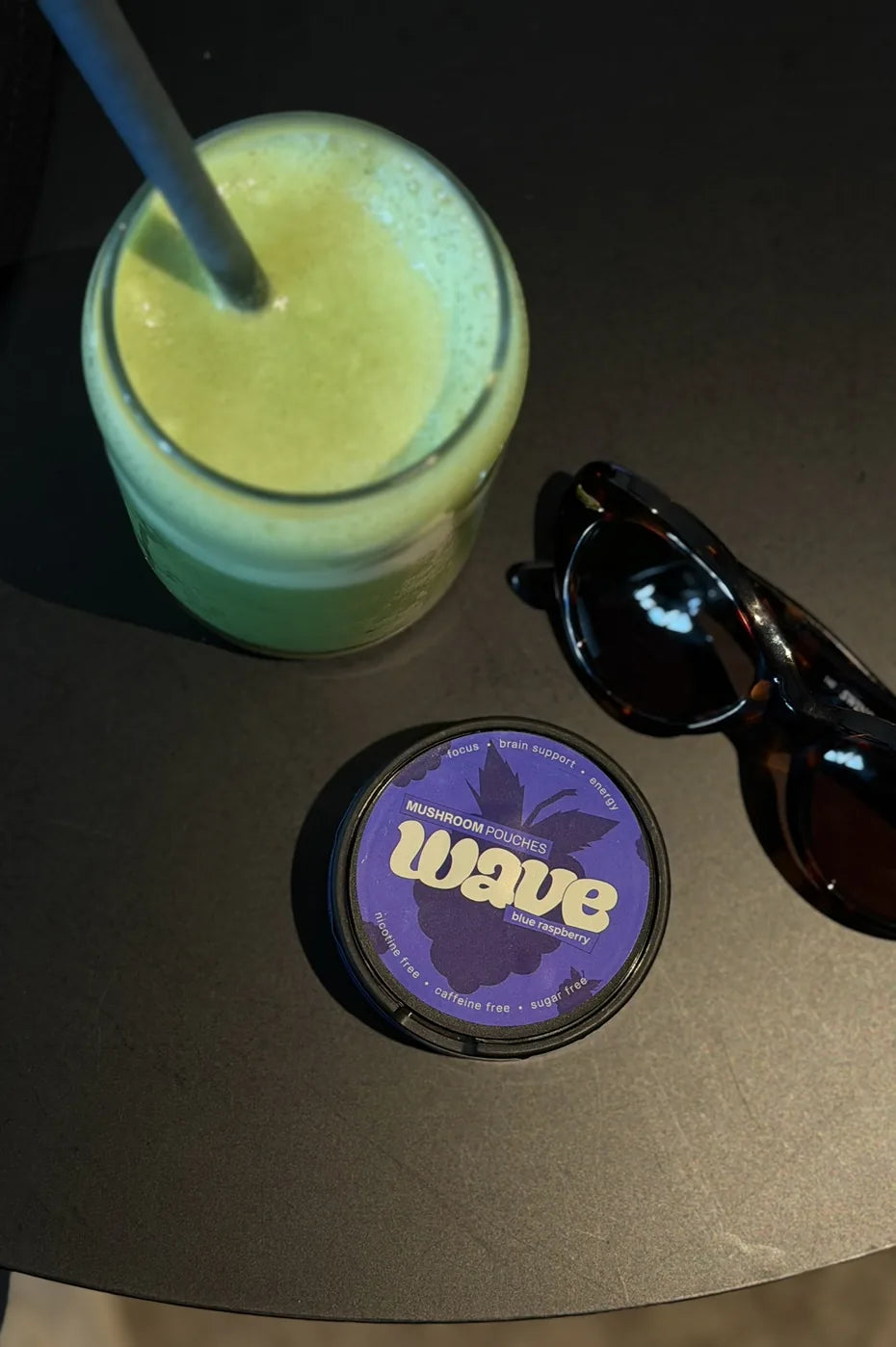 Blikje WAVE op een donkere tafel naast een groene smoothie en een zonnebril